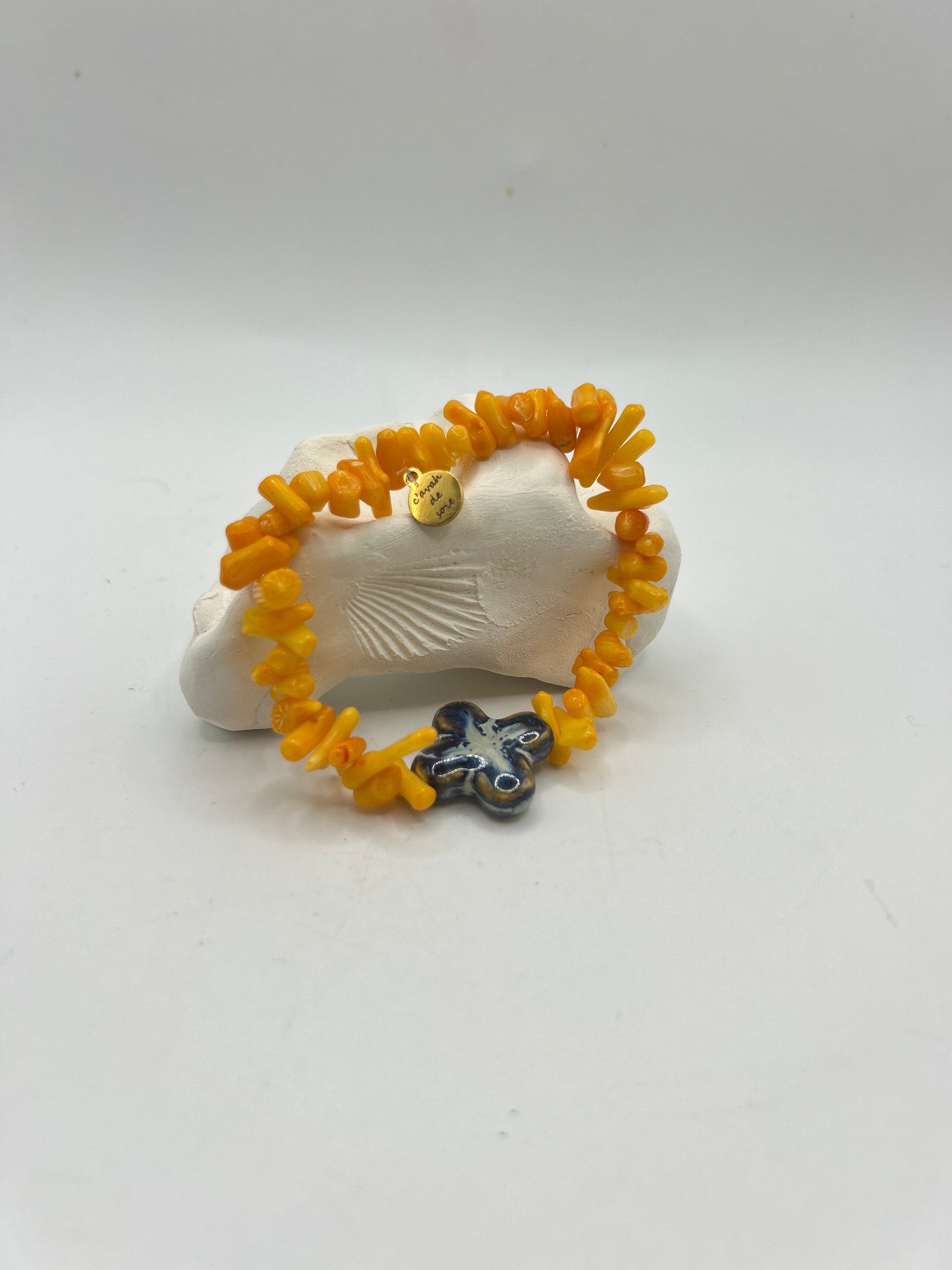 Bracelet artisanal composé d’éclats de corail orange naturel et d’une fleur en céramique émaillée bleue, création unique inspirée de la mer et du style bohème méditerranéen.