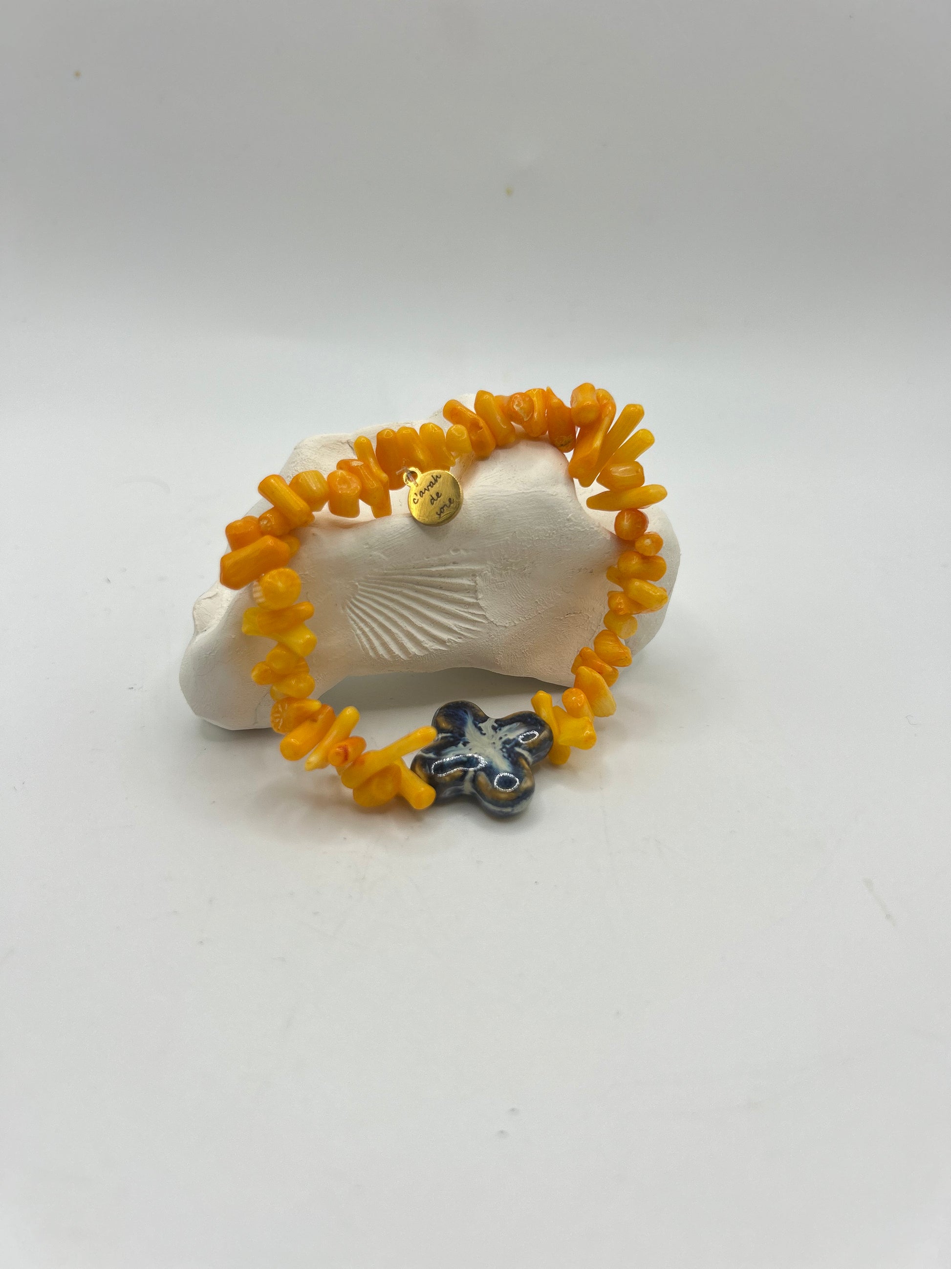 Bracelet artisanal composé d’éclats de corail orange naturel et d’une fleur en céramique émaillée bleue, création unique inspirée de la mer et du style bohème méditerranéen.