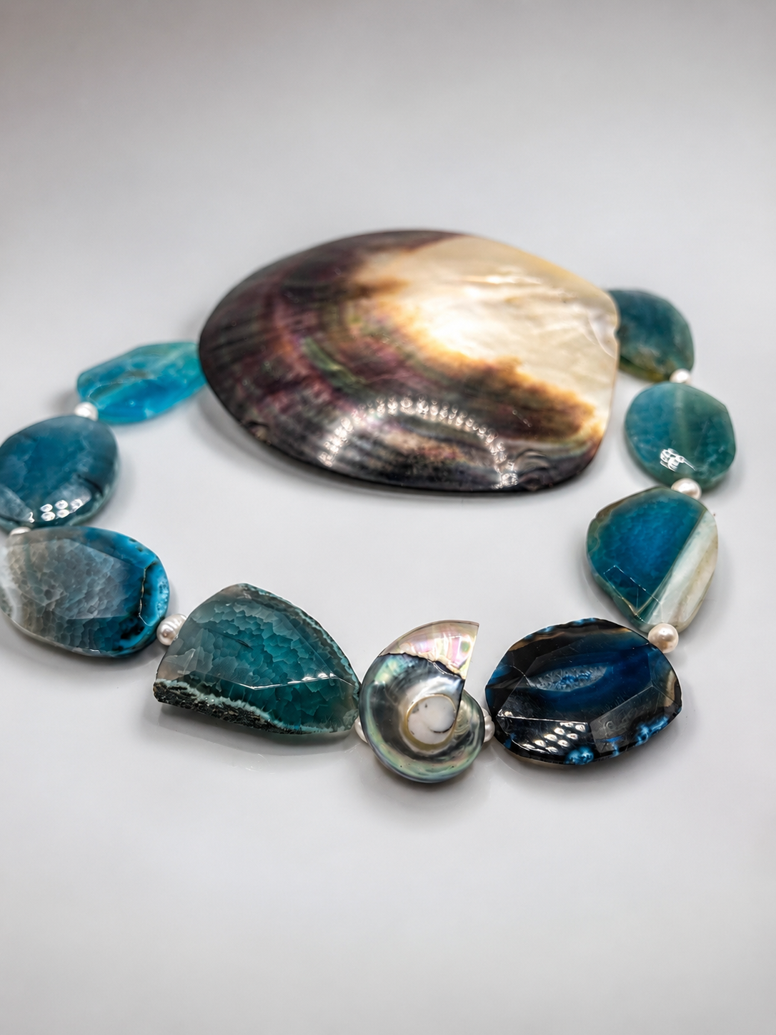 Collier artisanal en Agate bleue naturelle avec coquillage nautile bleu et blanc nacré en pendentif central, bijou inspiré de l’océan et du bord de mer.