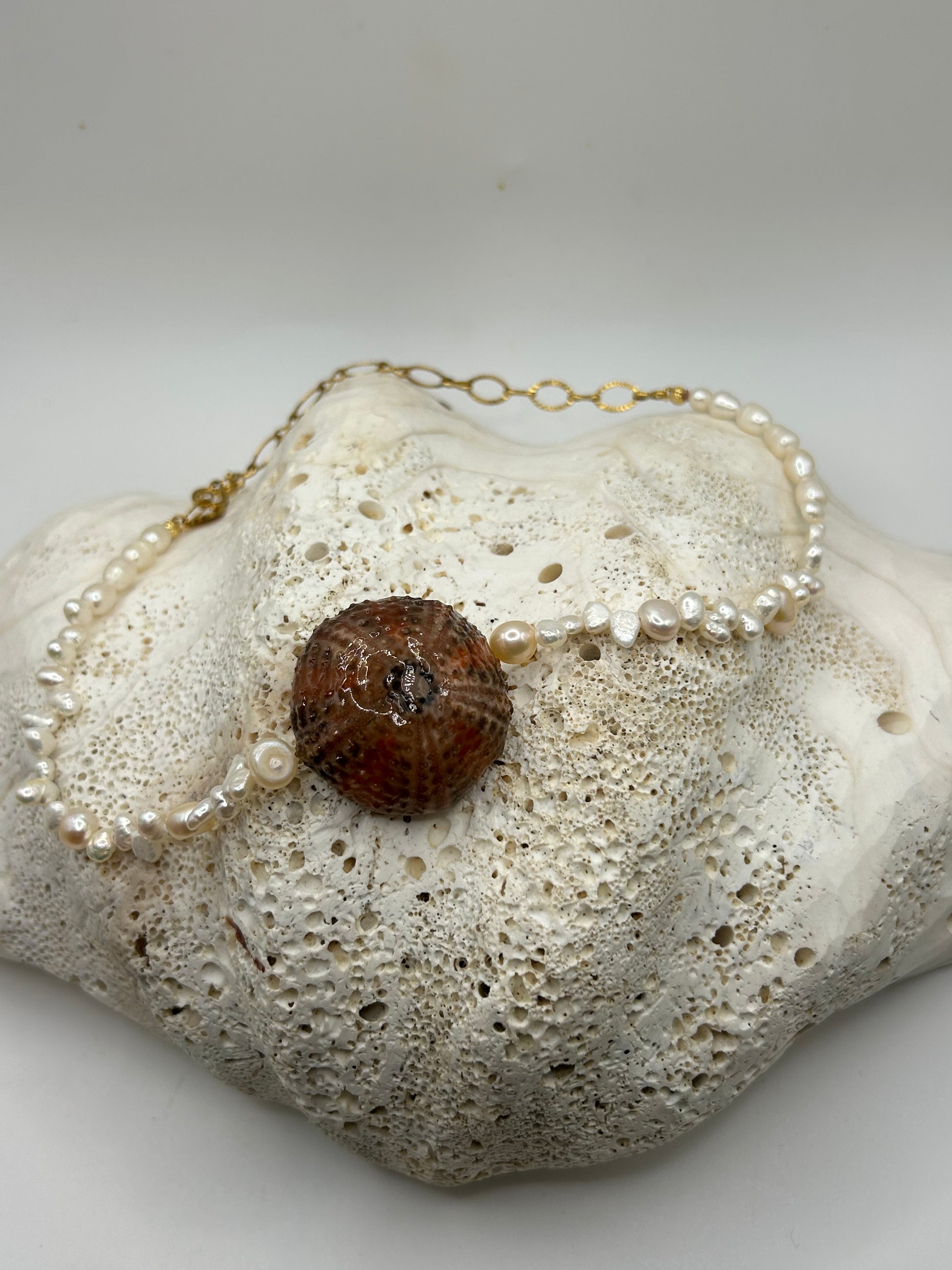 Collier artisanal avec oursin naturel orange et noir au centre et véritables perles de culture nacrées, création unique inspirée des trésors de l'océan.

