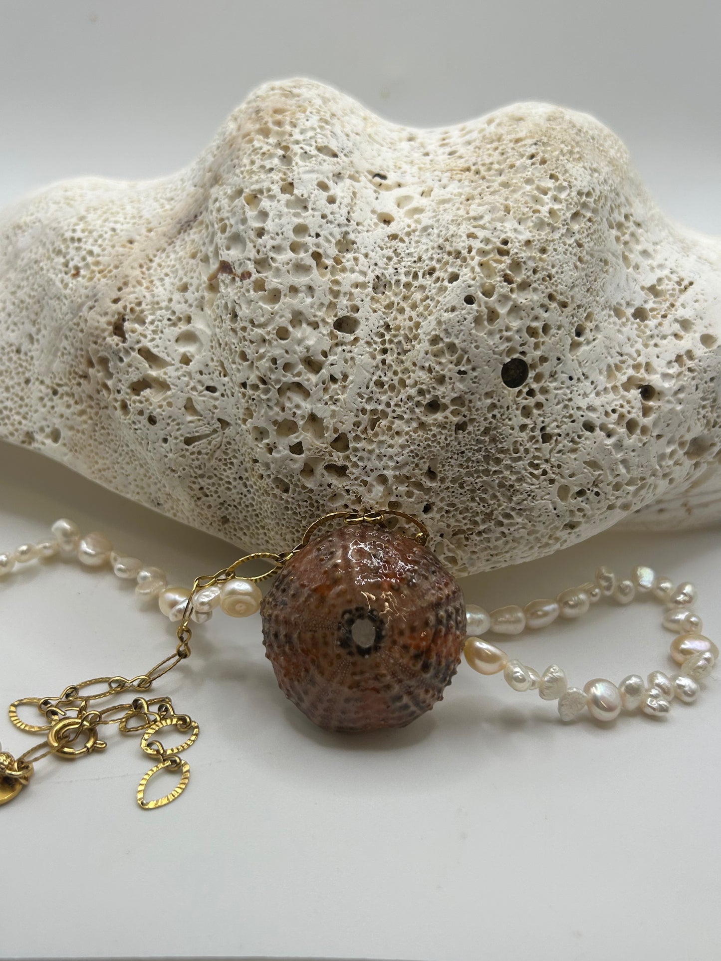 Collier artisanal avec oursin naturel orange et noir au centre et véritables perles de culture nacrées, création unique inspirée des trésors de l'océan.

